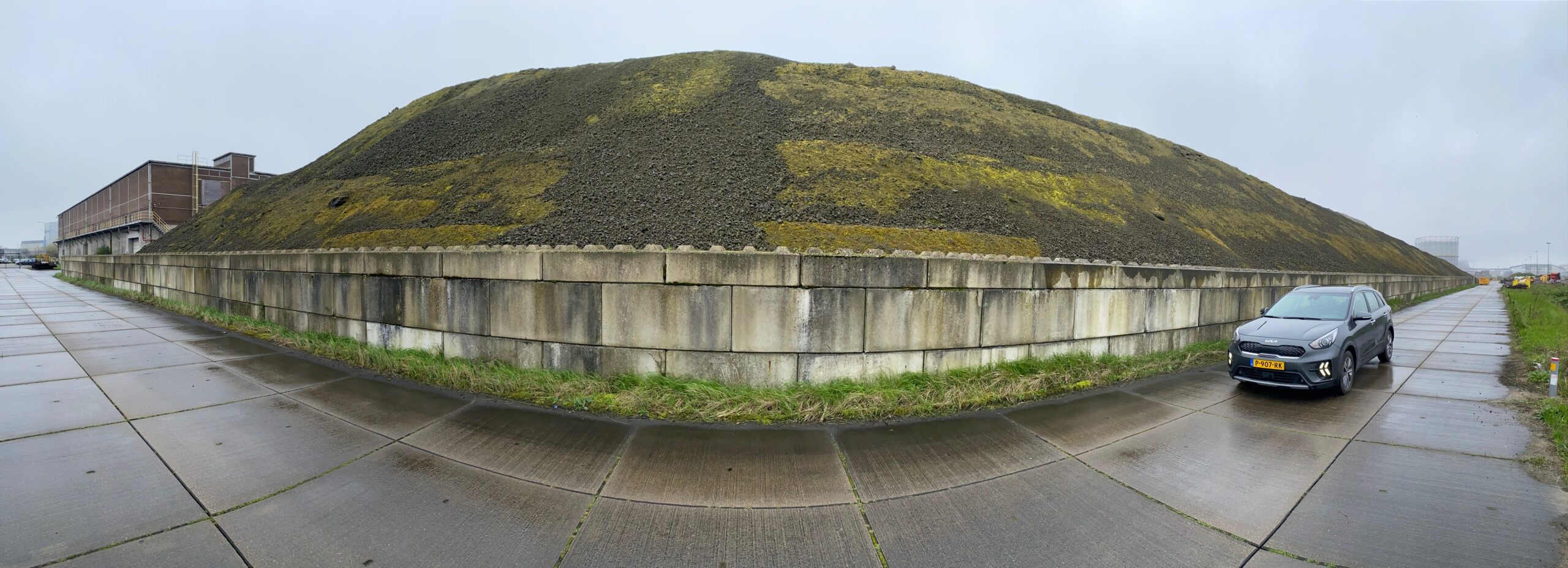 Panoramafoto van de staalslakkenberg aan de Mergelkade, met aan de rechterkant een auto van de OD NZKG